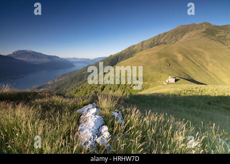 Sunbeam sulla chiesa di San Bernardo si illumina il paesaggio attorno alle acque blu del lago di Como a Alba, Musso, Lombardia, Italia Foto Stock