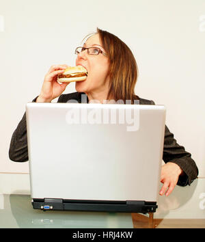 Gesch?ftsfrau bei der Arbeit am beisst Laptop in einen Burger - Business donna morsi in un burger durante l'utilizzo di laptop, Symbolfotos Foto Stock