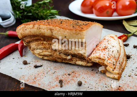 Un grande pezzo di pancetta cotta in forno con le spezie e le erbe su una carta con pomodori marinati. Un pasto di festa. Pasqua. Natale. Foto Stock