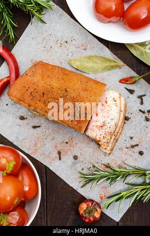 Un grande pezzo di pancetta cotta in forno con le spezie e le erbe su una carta con pomodori marinati. La vista dall'alto. Un pasto di festa. Pasqua. Natale. Foto Stock