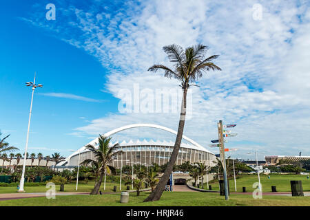 DURBAN, Sud Africa - 24 febbraio 2017: la mattina presto, pavimentato promenade, verde prato e alberi di palma contro Mosè Mabhida Stadium e il clou di colore blu Foto Stock