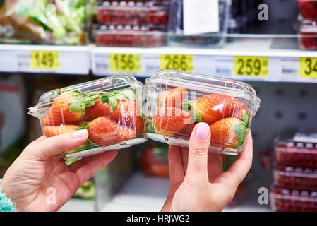 Le fragole nelle mani del compratore presso il negozio sullo sfondo di ripiani con prodotti Foto Stock