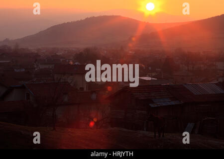 Verso il basso del sole sulle colline, piccolo villaggio di montagna sopra, rosso sunlights faling Foto Stock