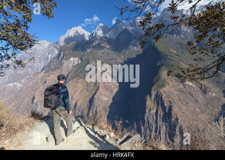 L'uomo escursionismo in Tiger salta in gola con il Jade Dragon Snow Mountain (Yulong Xueshan), Yunnan, Cina Foto Stock