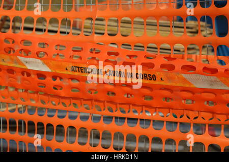 Di plastica arancione rete di sicurezza per delimitare la zona di una strada in costruzione sito con parole italiane significato ATTENZIONE LAVORI IN CORSO Foto Stock