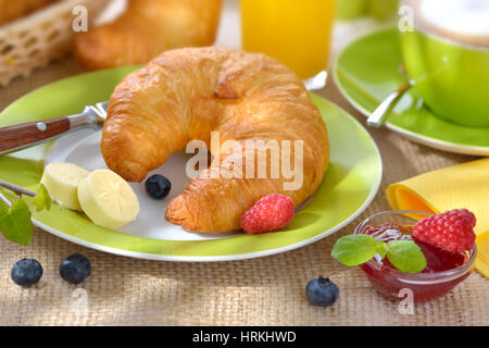 Tavolo per la colazione con una tazza di cappuccino e croissant freschi con burro e marmellata Foto Stock