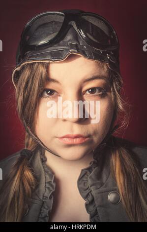 Ragazza indossando aviatore cappello e occhiali rende stupida espressione facciale dal forte vento Foto Stock