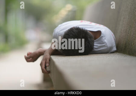 Uomo di dormire su una panca in calcestruzzo Foto Stock