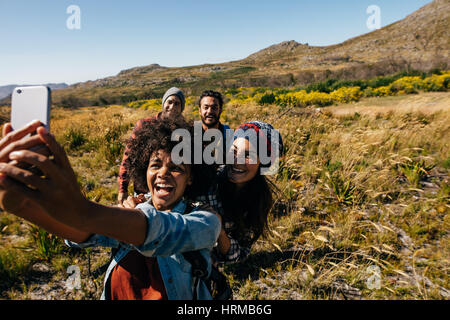 Gruppo di amici a piedi prendendo selfie in campagna. Giovani escursioni nel paese tenendo autoritratto con il telefono cellulare. Foto Stock