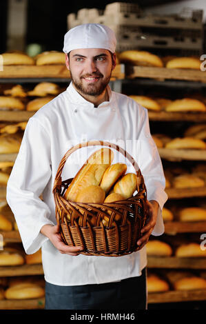Giovane uomo bello tenendo un paniere di beni cotti al forno su sfondo pane store Foto Stock