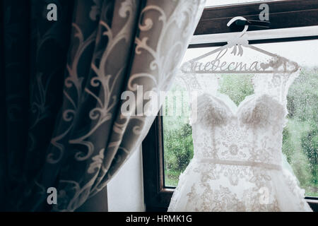 Abito da sposa appeso a una finestra con tende, close-up Foto Stock