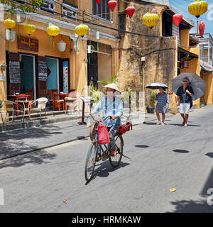 La donna corse in bicicletta in antica città di Hoi An. Quang Nam Provincia, Vietnam. Foto Stock