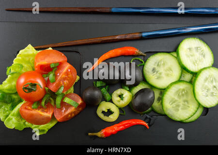 Bacchette e insalata di verdure su sfondo nero Foto Stock