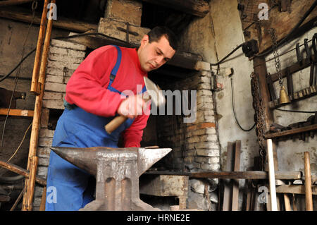 LUPENI, Romania - 19 Aprile 2012: Unidentified fabbro lavora su un oggetto di ferro con un martello durante un workshop Foto Stock