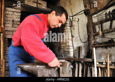 LUPENI, Romania - 19 Aprile 2012: Unidentified fabbro lavora su un oggetto di ferro durante un workshop Foto Stock