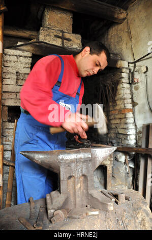 LUPENI, Romania - 19 Aprile 2012: Unidentified fabbro lavora su un oggetto di ferro con un martello durante un workshop Foto Stock