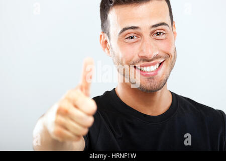 Sorridente giovane uomo che mostra pollice in alto Foto Stock