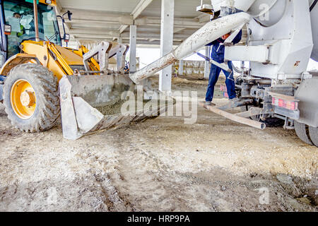 Betoniera carrello viene colata di calcestruzzo fresco nella benna di un escavatore in cantiere. Foto Stock