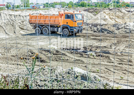 Vista attraverso un recinto di filo metallico su dumper che sta andando indietro per scaricare il terreno in corrispondenza del sito di costruzione. Foto Stock