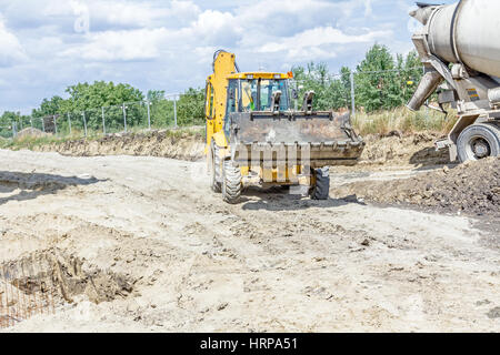 Escavatore è il trasporto di calcestruzzo fresco nel suo benna anteriore oltre il sito di costruzione. Foto Stock