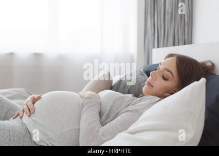 Femmine gravide di sdraiarsi su un letto e toccando il suo ventre. Foto Stock