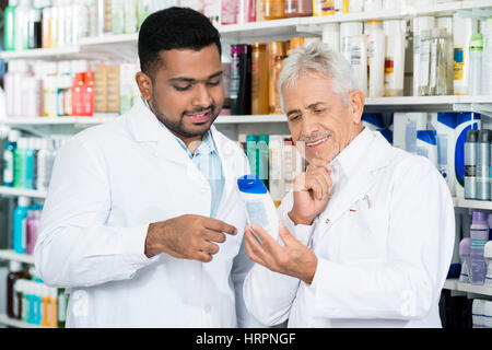 Sorridente farmacista maschio guardando alla bottiglia di shampoo permanente, mentre in farmacia Foto Stock