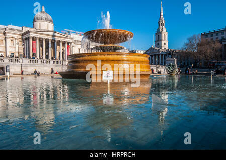 Fontana a Trafalgar Square, Londra, Regno Unito, con ghiaccio sull'acqua in inverno. Cielo azzurro e nitido Foto Stock