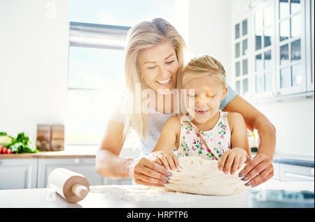 Graziosa bambina gli impasti con la madre a ridere con gioia come lei impara a cuocere, vista ravvicinata con un luminoso elevato la chiave di sfondo e copiare spac Foto Stock