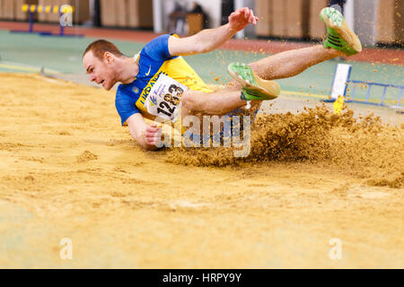 SUMY, Ucraina - 17 febbraio 2017: Serhiy Nykyforov sbarco nella buca di sabbia nel salto in lungo Qualification ucraino sulla pista coperta e campionato del campo 2 Foto Stock