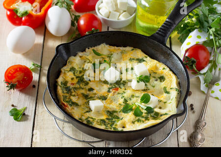 Frittata con peperoni, pomodori e formaggio feta in una ghisa padella su di un tavolo di legno. Il concetto di una sana nutrizione e dietetica. Il bulgaro cuis Foto Stock