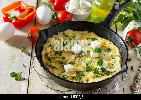 Frittata con peperoni, pomodori e formaggio feta in una ghisa padella su di un tavolo di legno. Il concetto di una sana nutrizione e dietetica. Il bulgaro cuis Foto Stock