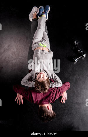 Vista superiore del figlio giacente sul retro del padre facendo ups push su nero Foto Stock