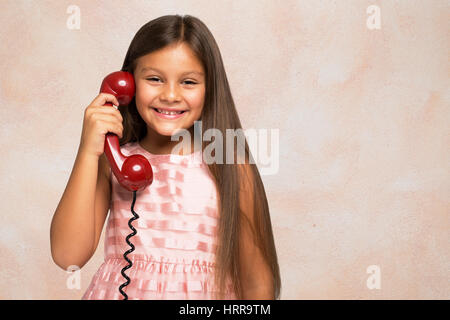 Sorridente bambina a parlare su un telefono vintage. Sfondo rosa Foto Stock