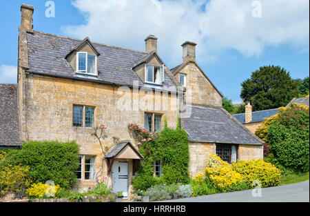 Inglese miele dorato marrone lapidato cottage con colorato giardino anteriore in un territorio rurale Cotswolds village, su un estate giornata di sole . Foto Stock