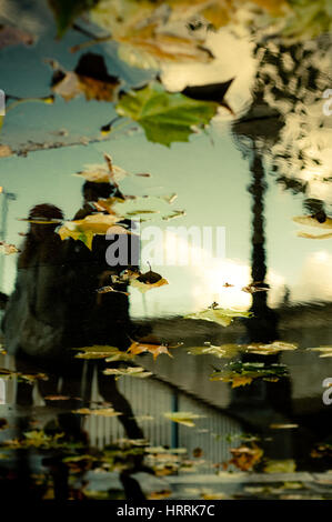 Sagome di persone a piedi si riflette nell'acqua durante il giorno di pioggia nella città Foto Stock