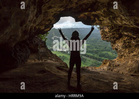 Giovane donna sta sollevando i bracci nella grotta di vittoria di finestra che si affaccia sul Rio Grande DE ARECIBO VALLEY PUERTO RICO Foto Stock