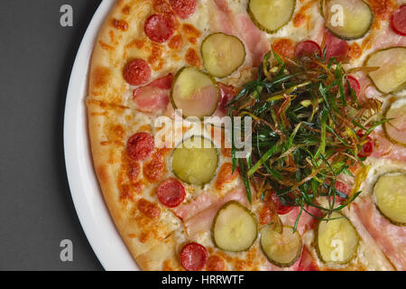 Vista superiore della parte di pizza con salsiccia, prosciutto, pancetta e cetriolo sottaceto decorate con fritto di cipolla verde Foto Stock