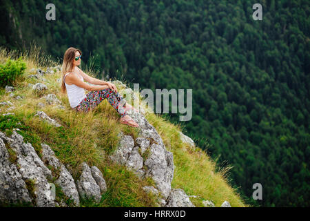 Donna bionda in sunglesses sedersi e rilassarsi alla fine della terra nel paesaggio affascinante in Montenegro Foto Stock