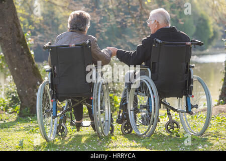 Coppia di anziani in carrozzina, tenendo le mani Foto Stock