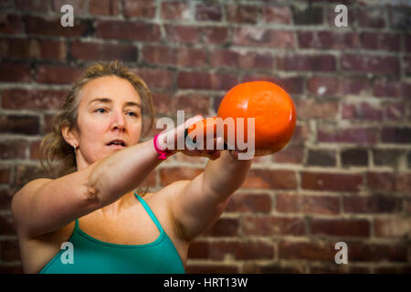 Una donna nel suo inizio 40's oscillazione un kettlebell mentre si lavora fuori. Foto Stock