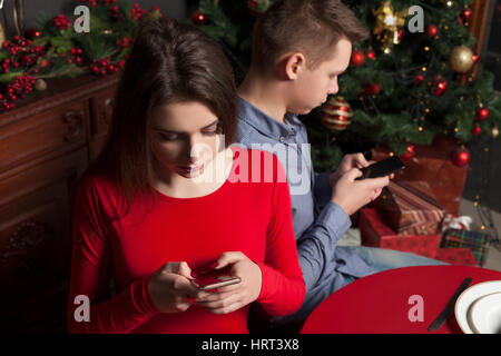 Coppia giovane utilizzando i telefoni cellulari. Ricco ristorante interno sullo sfondo Foto Stock