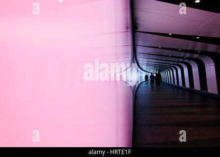 La riflessione di persone a piedi attraverso stile futuristico tunnel pedonale dotato di un LED luminoso integrato nella parete granaio uscita quadrata da Kings Cro Foto Stock