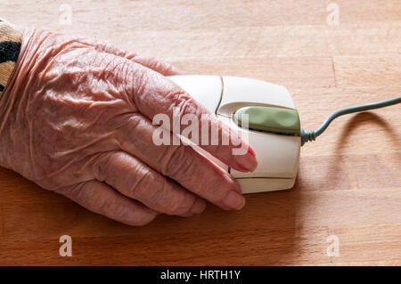 Mano di donna anziana eldearly usando il mouse del calcolatore. Senior che utilizza la tecnologia attuale. Foto Stock