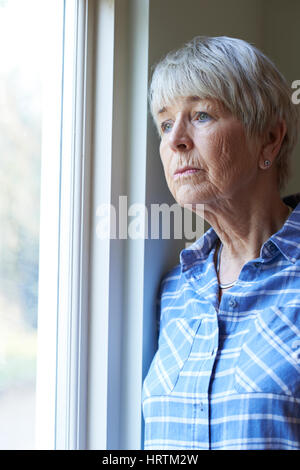 Senior donna che soffre di depressione guardando fuori della finestra Foto Stock