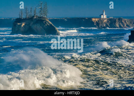 Onde enormi e laminazione di schiantarsi al tramonto Cove, Cape Arago faro in distanza, vicino a Charleston, Oregon, Stati Uniti d'America Foto Stock