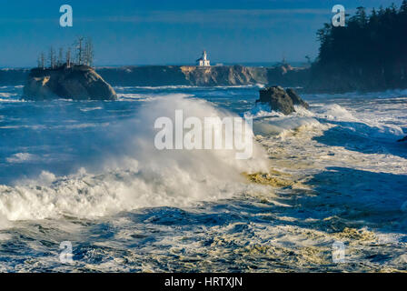 Onde enormi e laminazione di schiantarsi al tramonto Cove, Cape Arago faro in distanza, vicino a Charleston, Oregon, Stati Uniti d'America Foto Stock