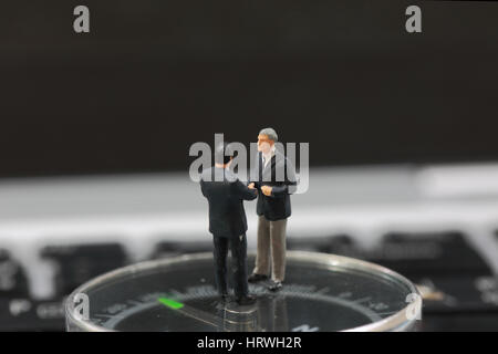 Messa a fuoco selettiva di imprenditore in miniatura handshake alzarsi sulla bussola background come impegno e lavoro di squadra concetto. Foto Stock