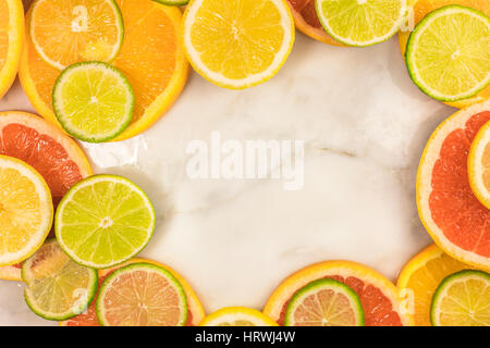 Un telaio vibrante costituito da succosa agrumi, su un marmo bianco texture, con copia spazio. Pompelmo, calce, limone e fettine di arancia Foto Stock