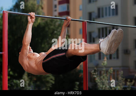 Uomo Fitness facendo gli allenamenti di stomaco sulla barra orizzontale all'esterno. Tirando sulla barra. L Uomo nel breve nero e bianco sneakers. Abs. Uno stile di vita sano. Foto Stock