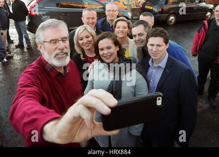 Sinn Fein Michelle O'Neill (centro sinistra), Mary Lou McDonald (centro) e Gerry Adams (sinistra) posa per una selfie nella parte anteriore del Bobby Sands murale dopo post elezione conferenza stampa al Sinn Fein sede a Belfast. Foto Stock